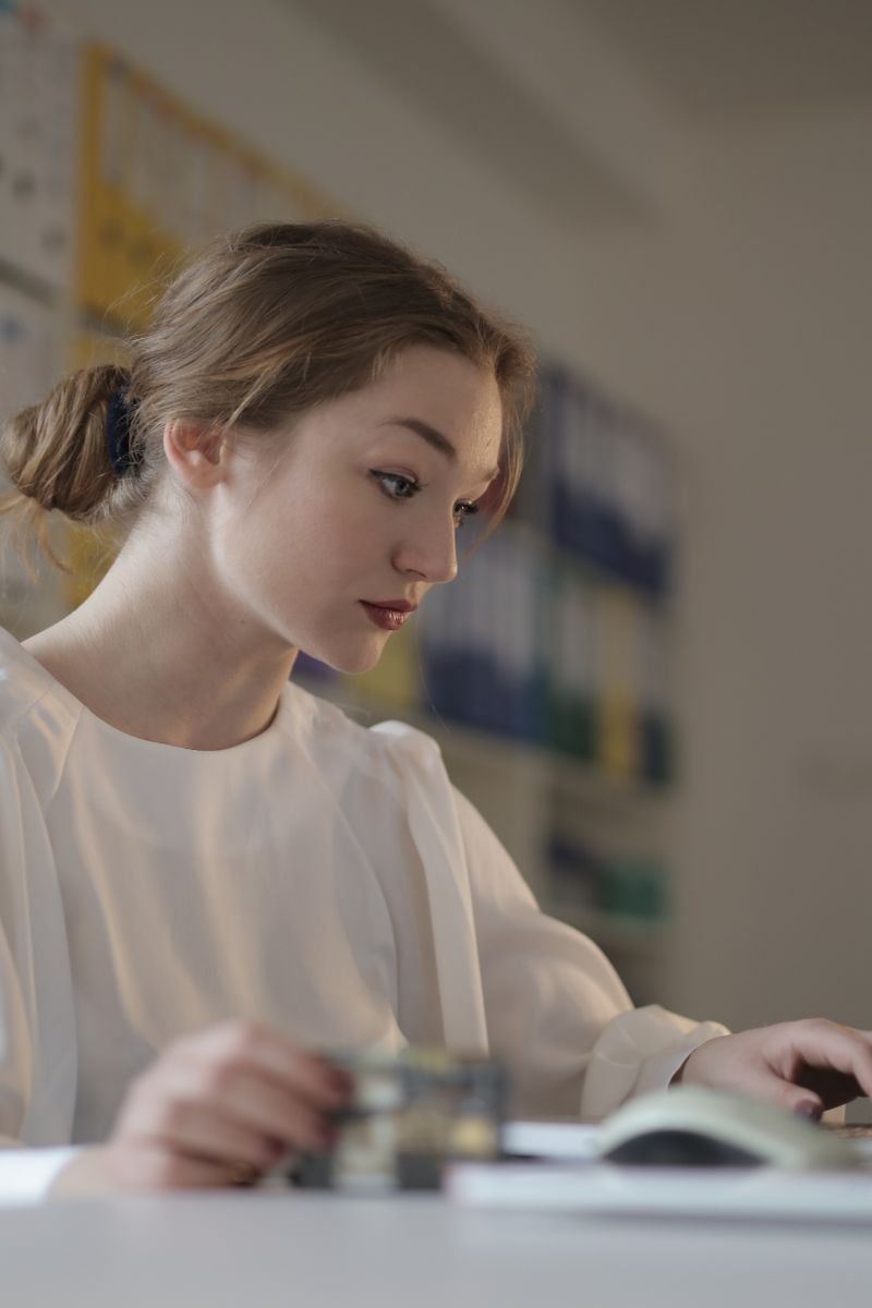 Focused woman in white working on a laptop in a modern office setting.